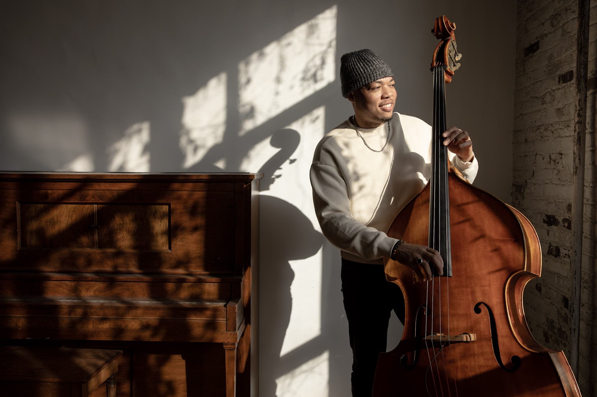 Bassist with an upright bass in a sunlit studio.